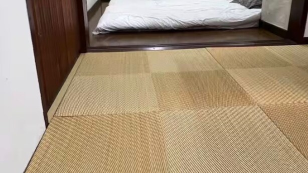 Una stanza piccola e compatta con un letto singolo, una testiera in legno e un pavimento in tatami.