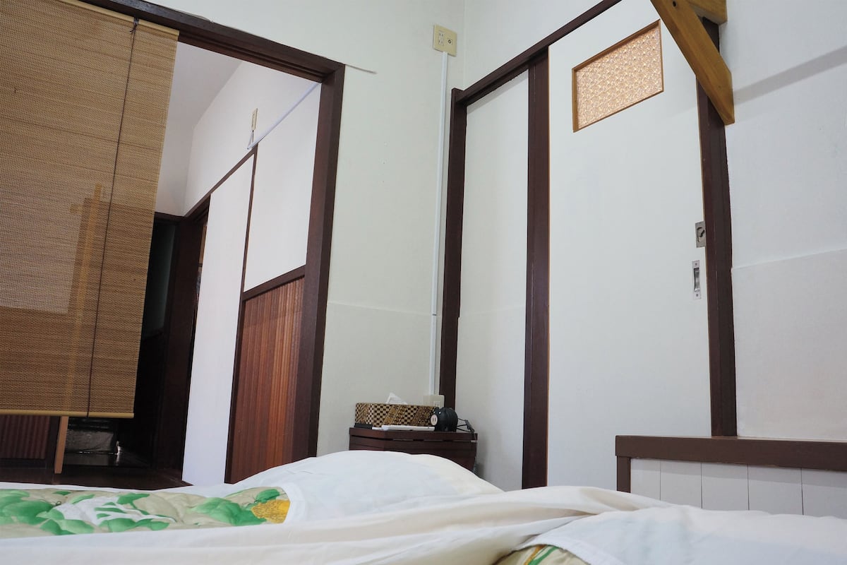 Une chambre à coucher comprenant un lit, une armoire en bois, une petite table de chevet et une étagère fixée au mur.