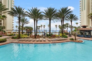 A resort pool area with multiple lounge chairs, palm trees, and a view of the ocean. - New! Ground Floor! No Elevators Needed! Beachfront! (Panama City Beach)
