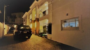 A narrow, paved alleyway leading to a multi-story building with a car parked on the left. - Morning Side Suites and Spa VI (Lagos)