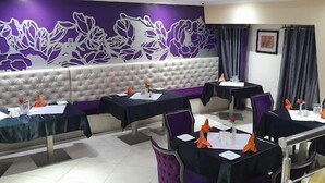 A restaurant with a purple floral wall design, multiple tables with chairs, and a cushioned bench area. - Morning Side Suites and Spa VI (Lagos)
