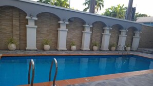A swimming pool with a tiled deck, surrounded by a low wall with columns and potted plants. - Morning Side Suites and Spa VI (Lagos)