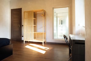 A room with a wardrobe, a bed, a desk, and a view through a glass door.