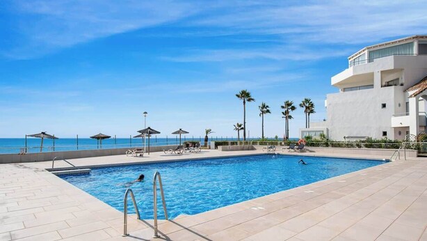 A swimming pool with a view of the ocean, surrounded by palm trees and lounge chairs.