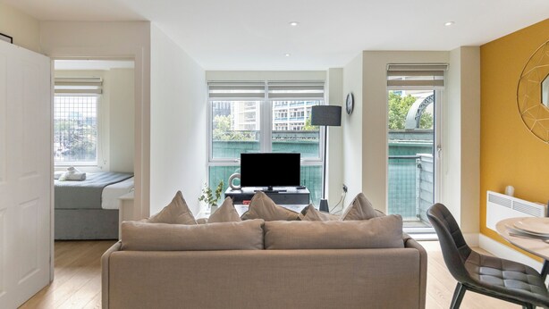 A modern living room with a sofa, a television, and a dining area.