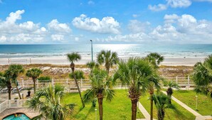 A beach view with palm trees, a pool, and a fence.
