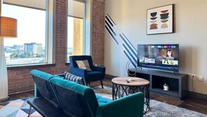A modern living room with a large TV, a sofa, a chair, and a view of the city.