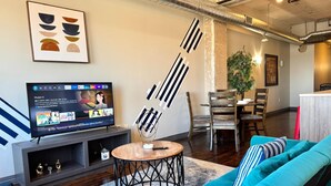 A modern living room with a teal sofa, a TV on a stand, and a decorative wall piece.