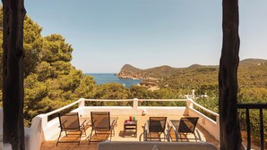 Una terraza al aire libre con vistas al mar y a las colinas, amueblada con sillas y una mesa.
