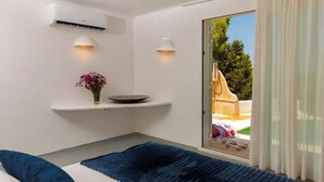 Un dormitorio con cama, una mesita de noche con un florero y aire acondicionado de pared, con vistas al exterior a través de un ventanal corredero.