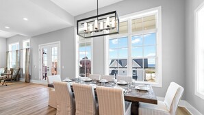 A spacious dining area with a large table, six chairs, and a modern chandelier.