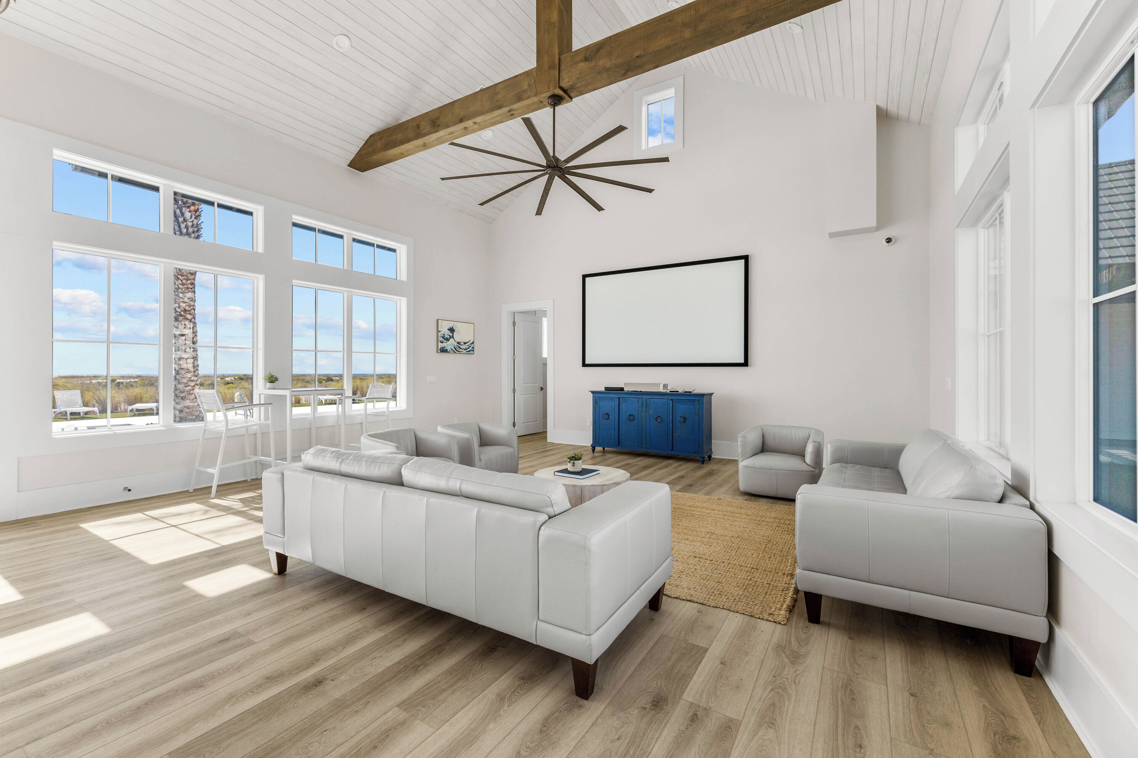 Un salon spacieux avec un grand canapé d’angle blanc, un meuble bleu et un ventilateur de plafond.