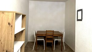 A small dining area with a wooden table and four chairs, a white shelf unit, and a white wall with a black picture frame. - Beautiful apartment 27b near Mainz University Hospital (Mainz)
