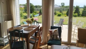 En matplats med ett bord för fyra personer, en soffa och utsikt över en trädgård genom stora skjutdörrar.