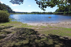 En sjö med en sandstrand och en person som paddlar i vattnet.