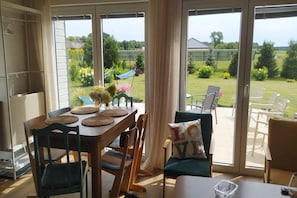A room with a dining table set for four, a sofa with a cushion, and a view of a garden through large sliding glass doors.