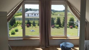 Ett rum med ett stort fönster, en gardin och ett litet runt bord.