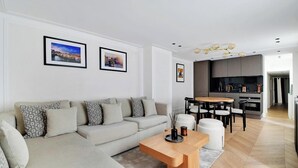 A modern living room with a sofa, coffee table, and dining area. There are framed pictures on the wall and a kitchen in the background. - AN IDEAL BASE FOR YOUR PARISIAN ADVENTURE, LOCATED AT RUE JACOB - SAINT GERMAIN (Paris)