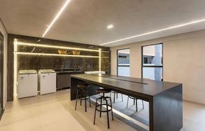 A modern kitchen with a long island, bar stools, and built-in appliances. - Beach Haus by Azzure Homes (João Pessoa)
