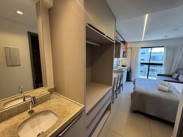 A modern hotel room with a bathroom, a kitchenette, a bed, and a large window. - Beach Haus by Azzure Homes (João Pessoa)