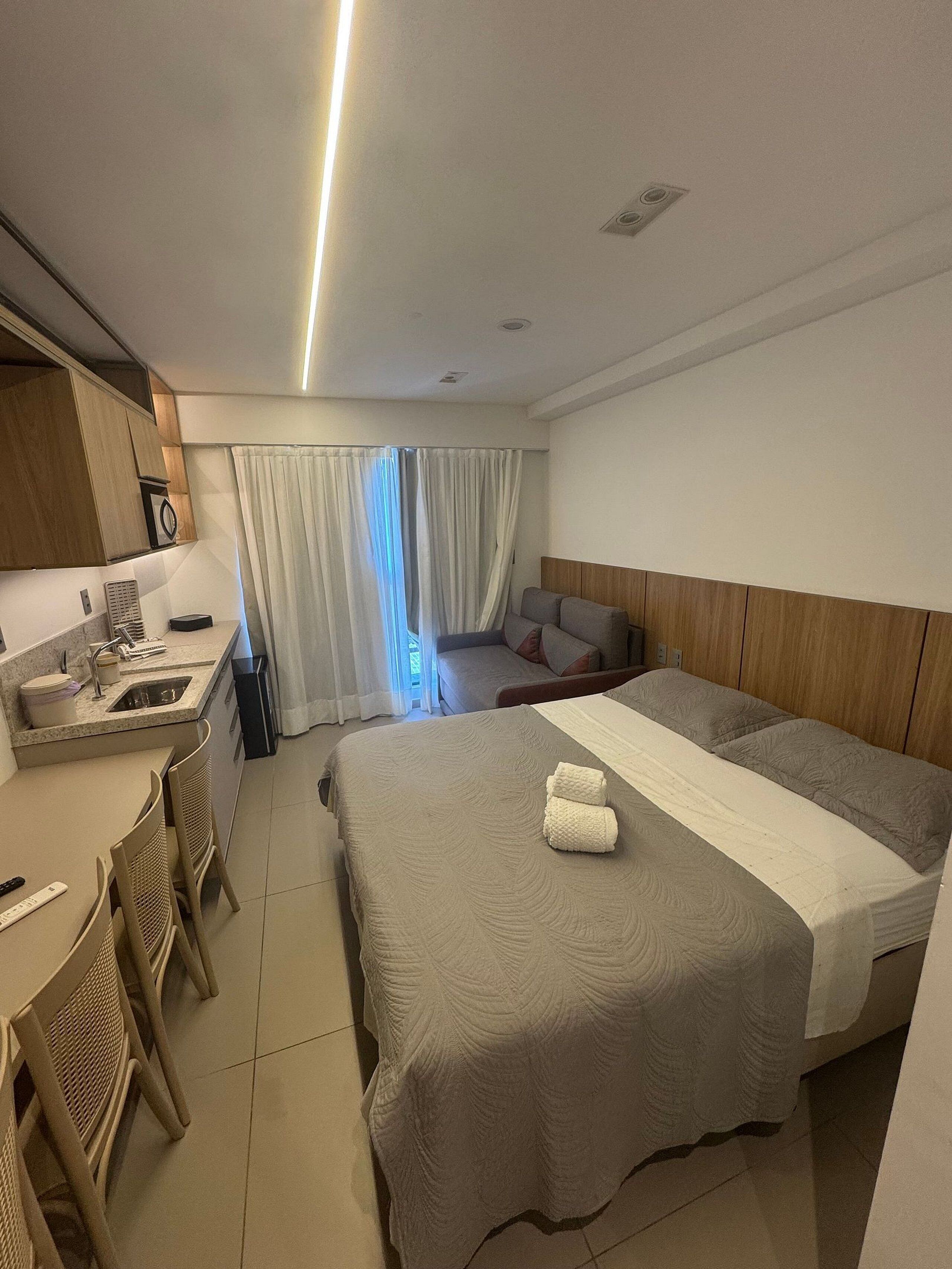 Une chambre d’hôtel avec un lit, un bureau, une chaise, un canapé et une fenêtre avec des rideaux.