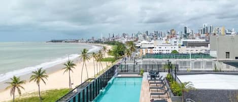 Une piscine sur le toit offrant une vue sur la ville, avec des palmiers et une plage à proximité.
