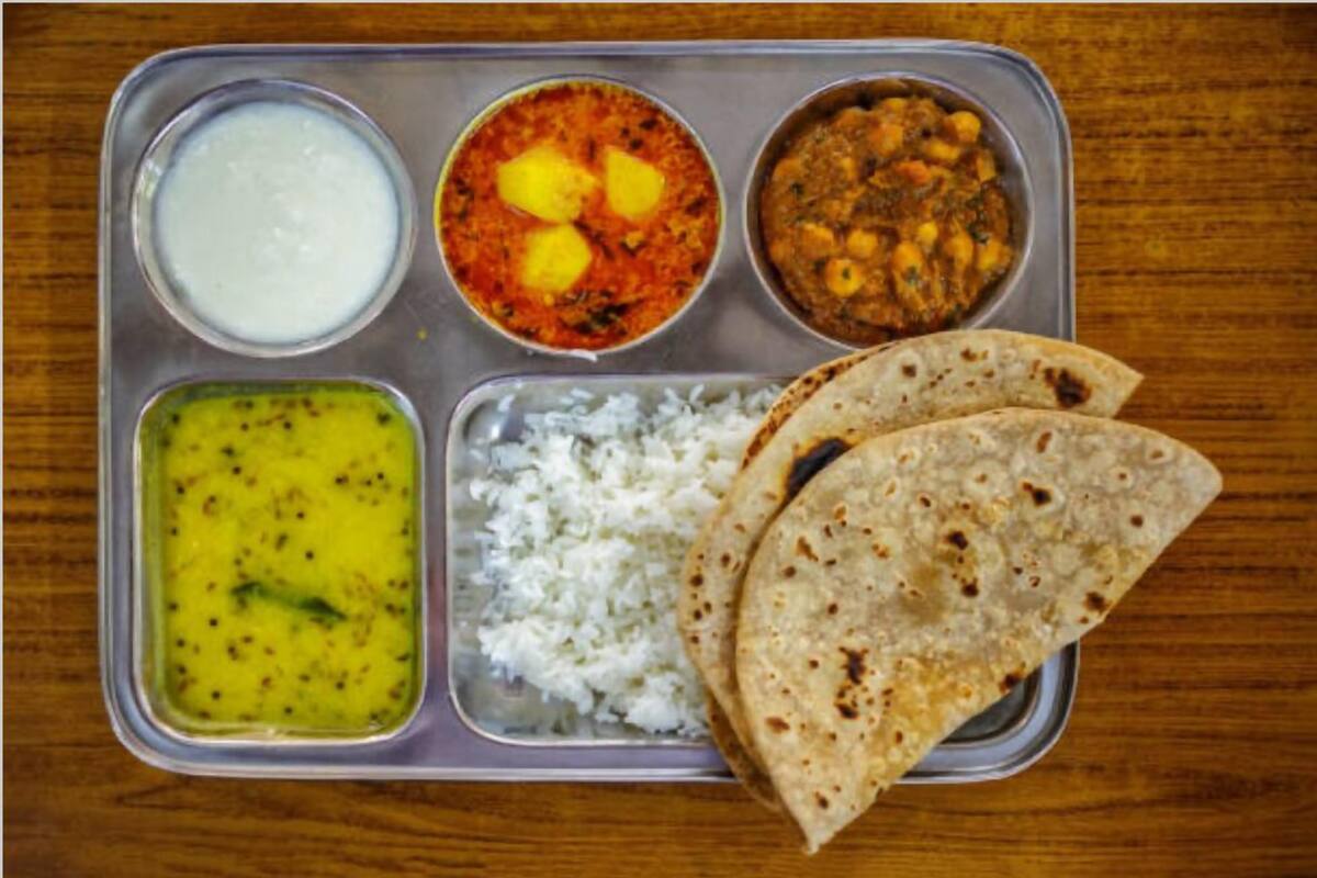 A meal tray with rice, two types of curry, a yogurt dish, and two pieces of flatbread.