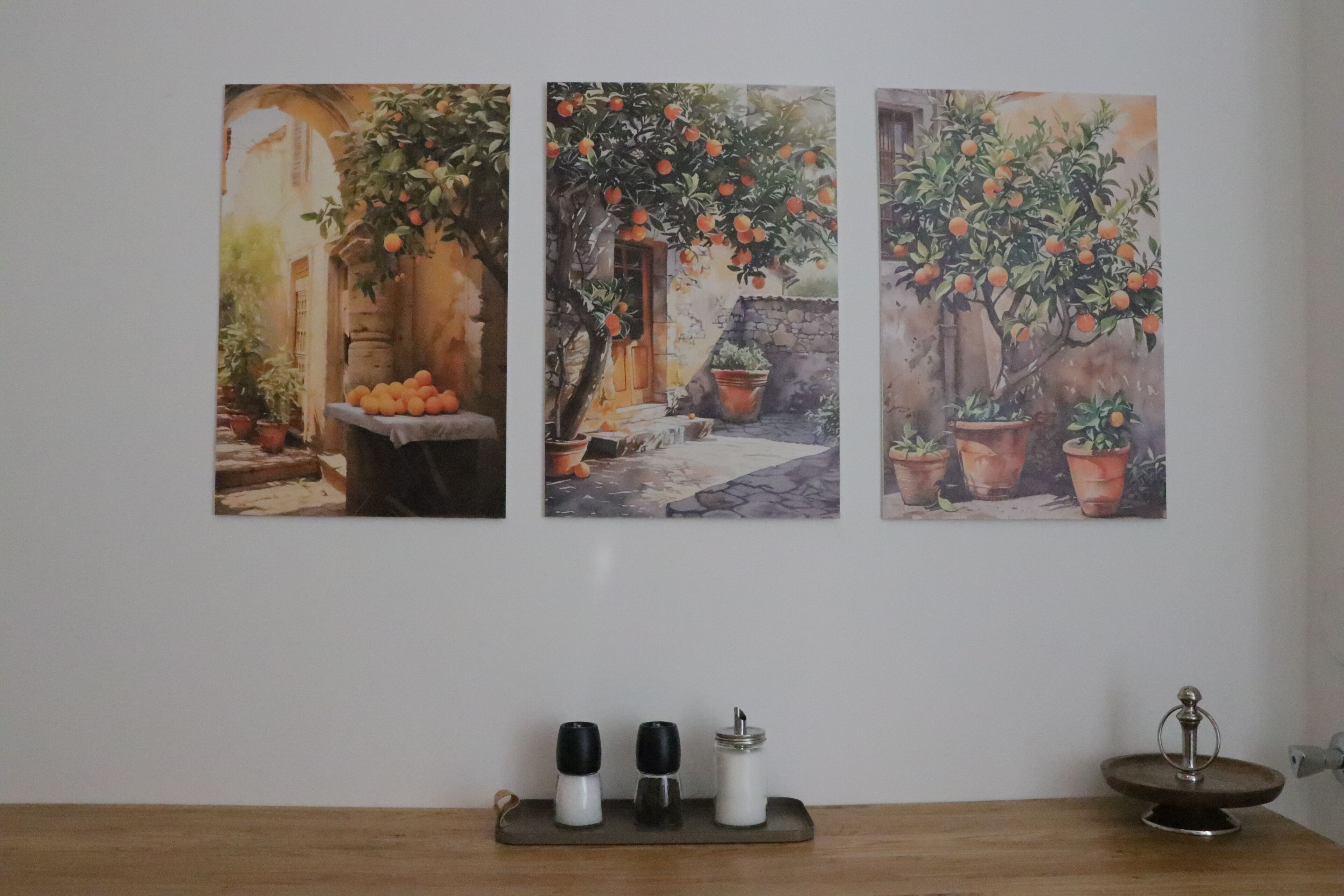 A wall with three paintings of orange trees and a wooden table with salt and pepper shakers.