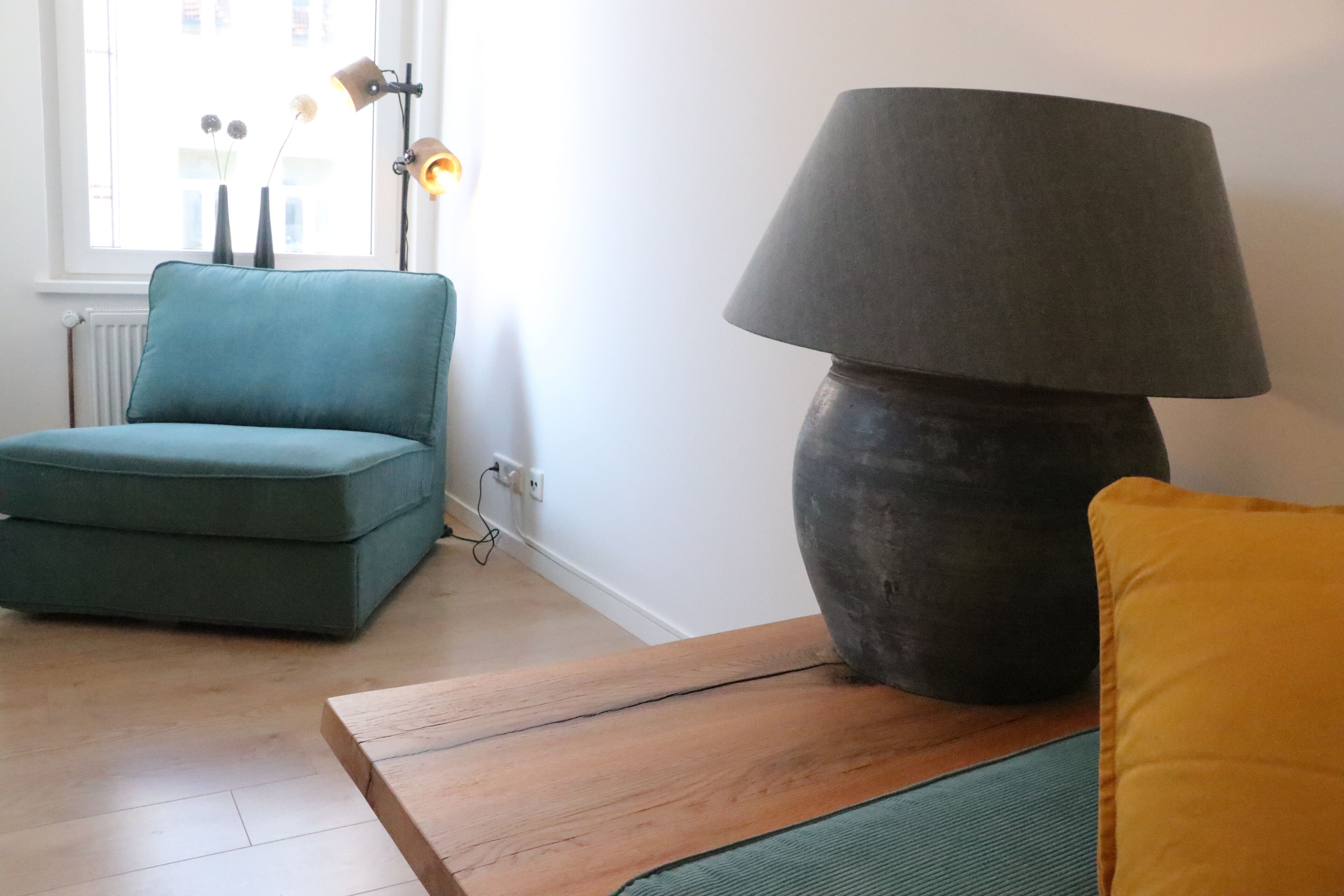 A room with a teal armchair, a large grey lamp, and a wooden table.