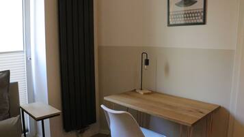 Een kamer met een houten bureau, een witte stoel, een zwart gordijn, een tafeltje en een poster aan de muur.
