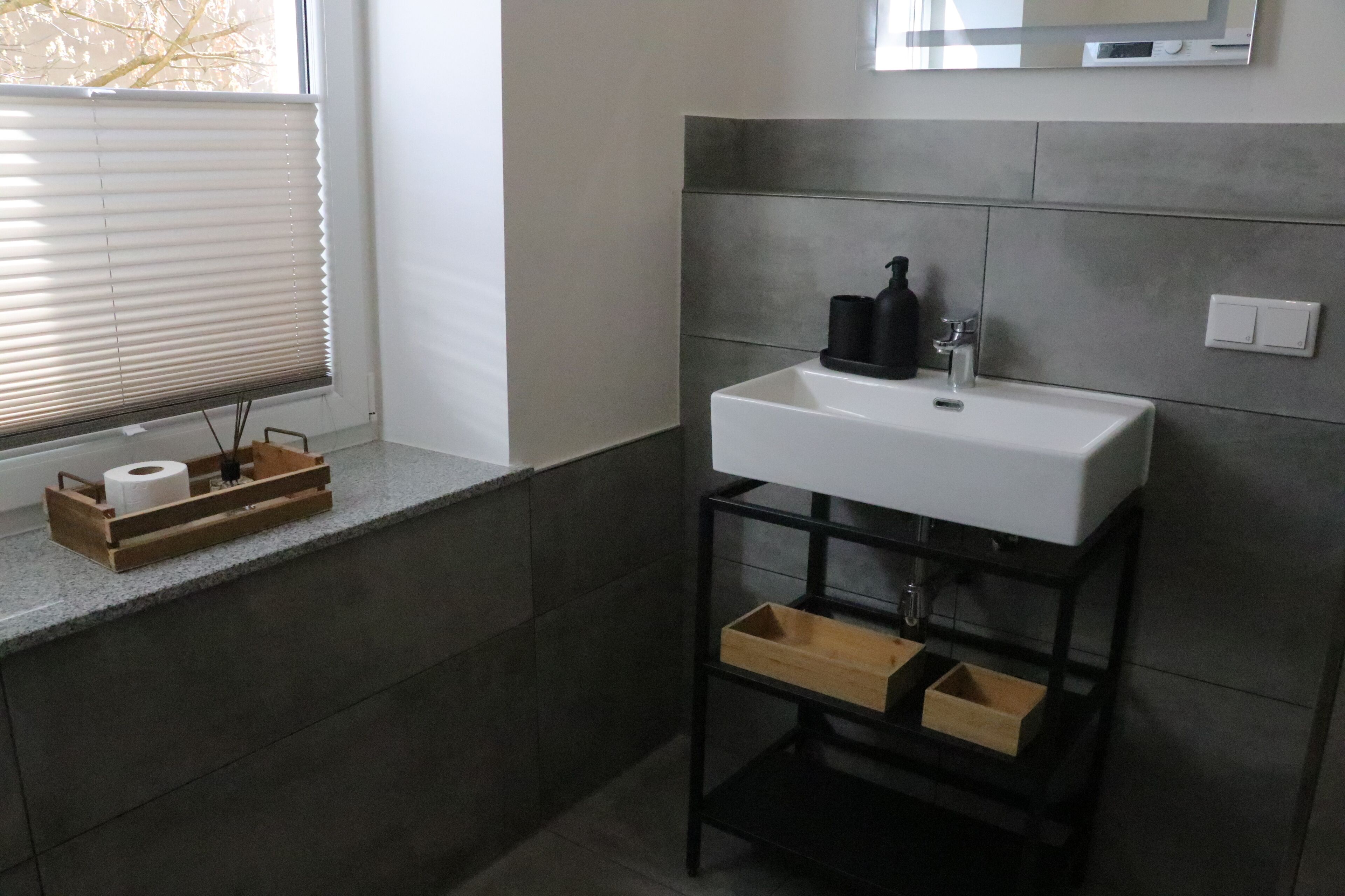 A bathroom with a white sink, a mirror above it, and a window with blinds.