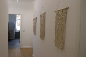 Ein Flur mit drei Wandteppichen aus Makramee, im Hintergrund eine Küche und ein Holzboden.