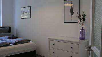 A bedroom with a bed, a dresser, a framed picture, and a vase with flowers.