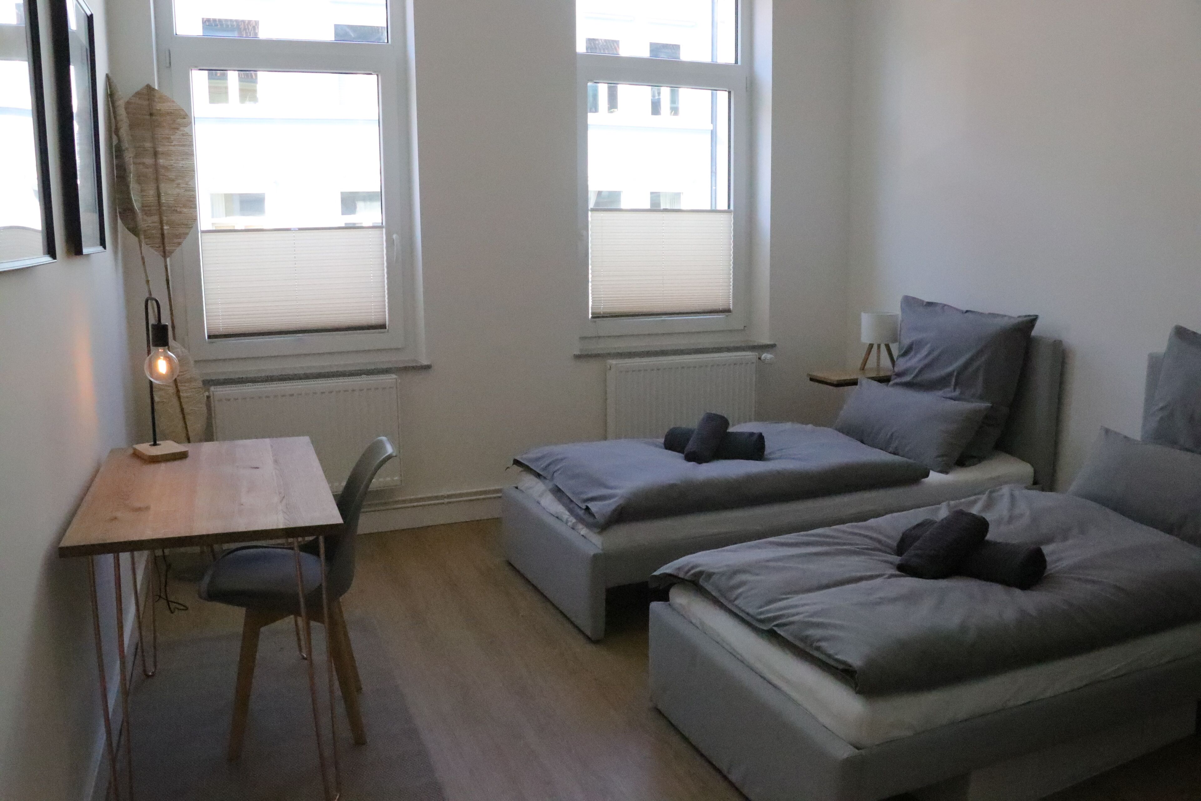 Une chambre avec deux lits simples, un bureau, une chaise et un radiateur.