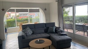 A modern living room with a sectional sofa, a round coffee table, and large windows offering a view of the outside. - Vacation apartment Wintersun (Bad Mergentheim)