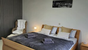 A bedroom with a wooden bed, a chair, a nightstand, and a wall-mounted lamp. - Vacation apartment Wintersun (Bad Mergentheim)