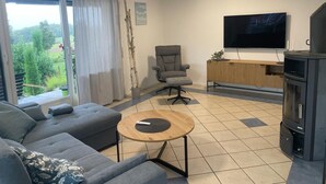 A modern living room with a grey sofa, a round wooden coffee table, a grey armchair, a TV, and a fireplace. - Vacation apartment Wintersun (Bad Mergentheim)