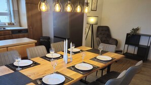 A modern dining room with a long wooden table, grey upholstered chairs, and a unique light fixture above. - Vacation apartment Wintersun (Bad Mergentheim)
