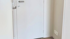 Una porta bianca con maniglia argentata e una serratura, pavimento in legno e una parete con tre decorazioni in legno.