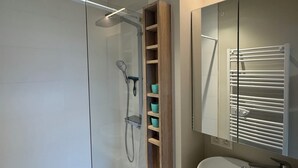 Un bagno moderno con box doccia in vetro, uno scaffale di legno con tazze color acquamarina, un lavandino bianco e uno specchio con porta asciugamani.