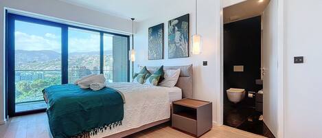 A modern bedroom with a large bed, a nightstand, and a view of the city through large windows.