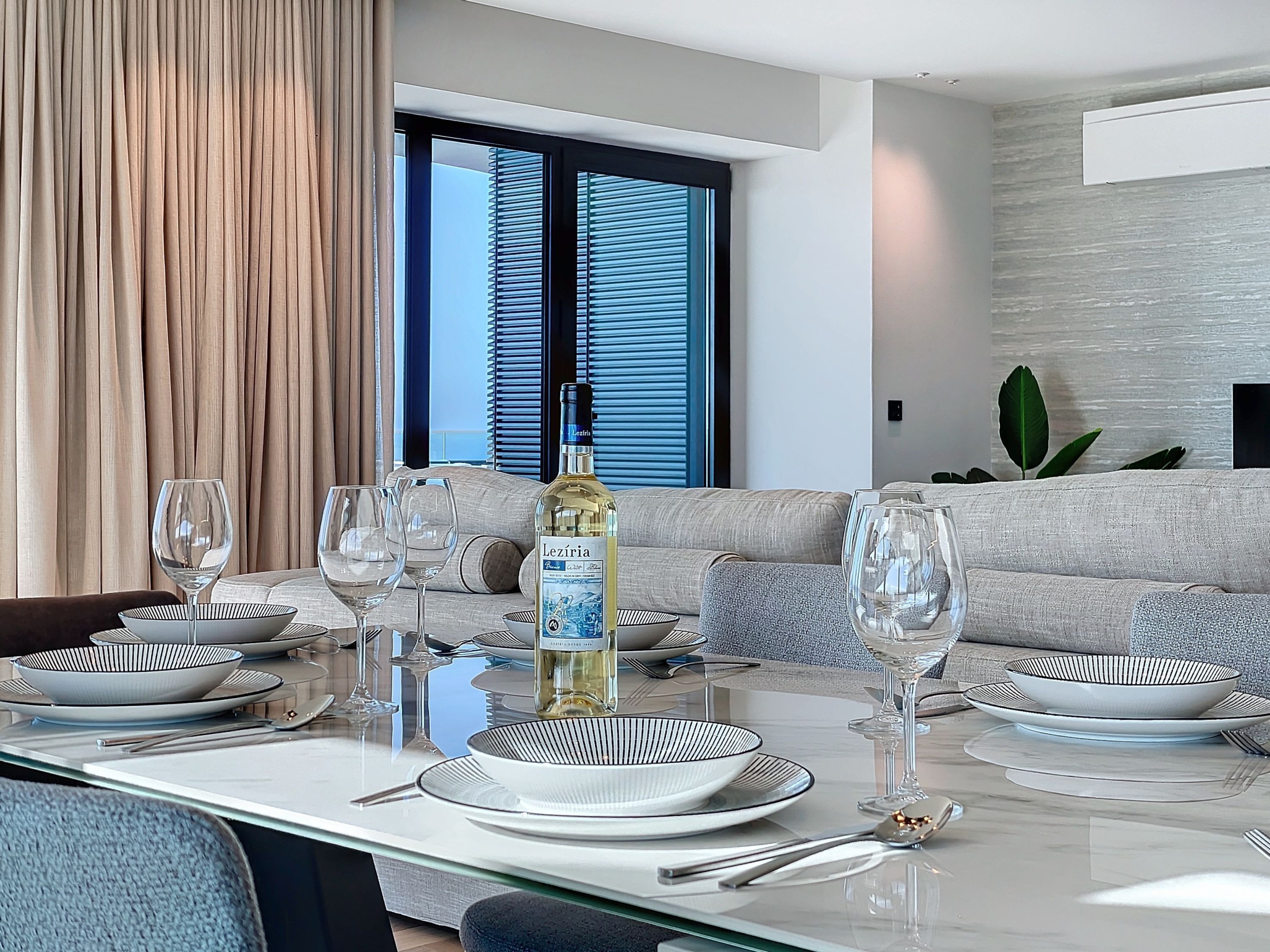 Un coin repas avec une table dressée pour six personnes, une bouteille de vin blanc et un canapé en arrière-plan.