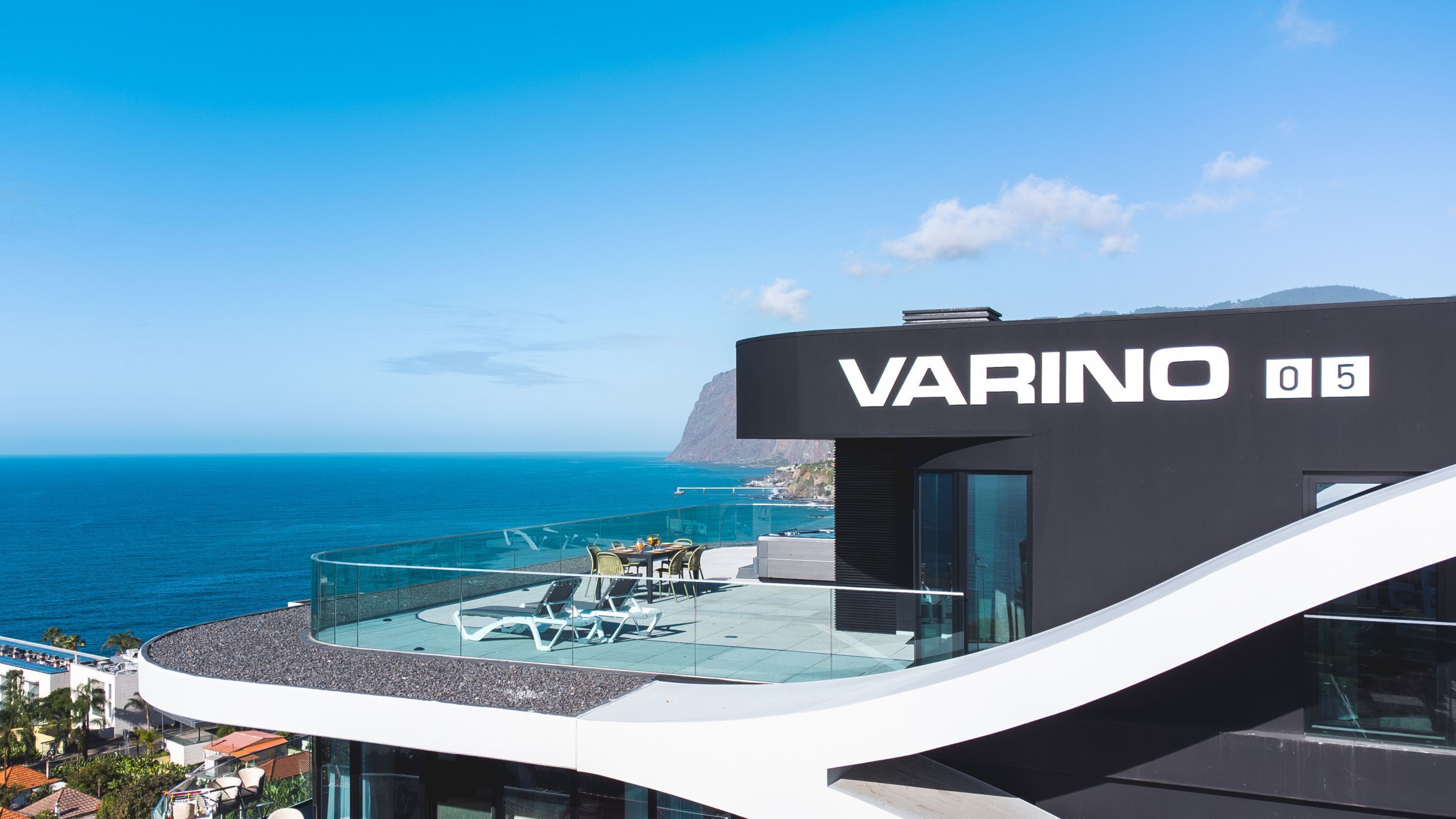 Un edifici modern amb terrassa a la teulada que domina l'oceà. L'edifici té un rètol que diu "VARINO 05".