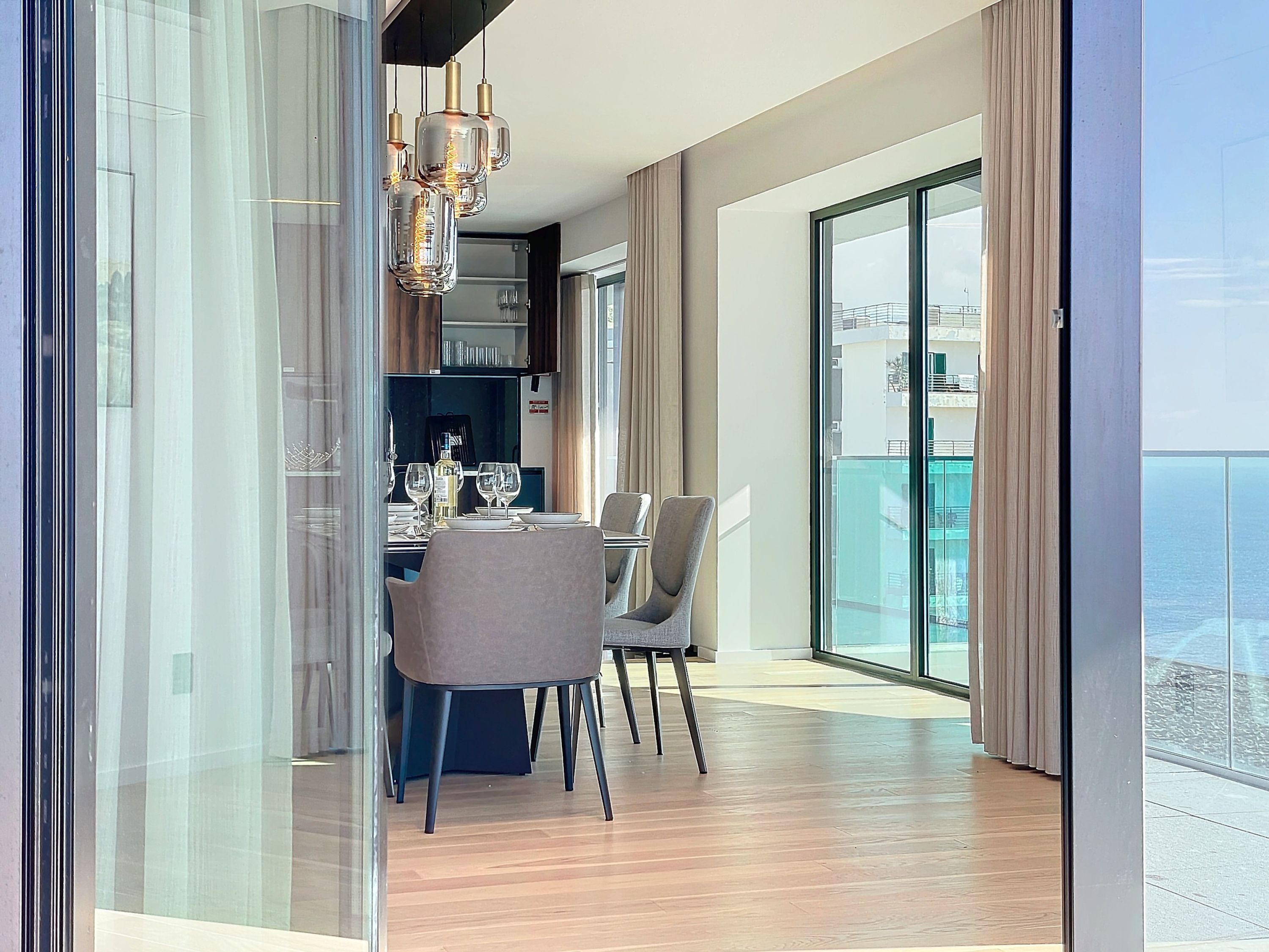 Un espace de restauration moderne avec une table dressée pour deux personnes, un lustre et une vue sur la ville grâce à de grandes fenêtres.