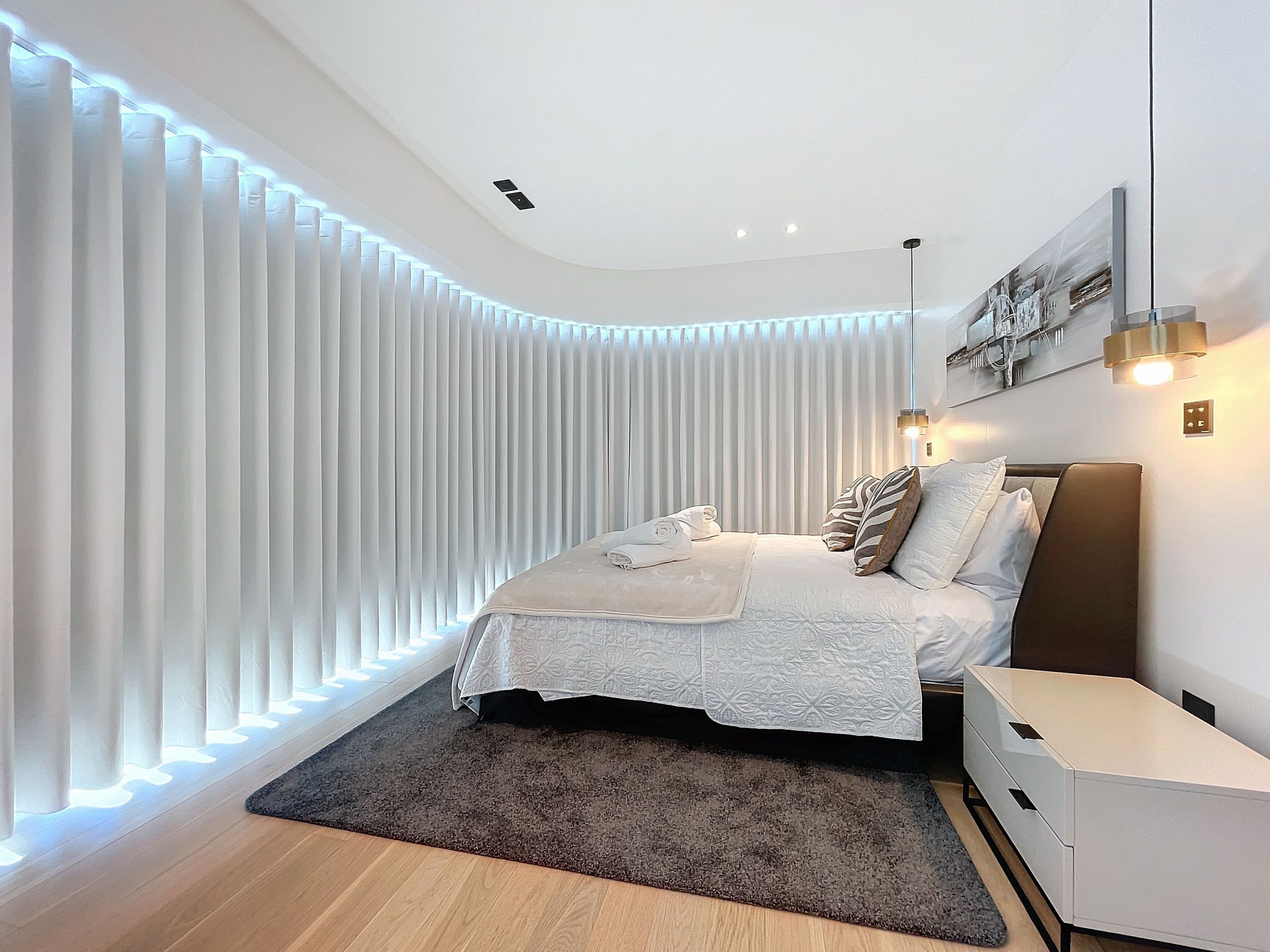 A modern bedroom with a bed, bedside tables, and a large window with vertical blinds.