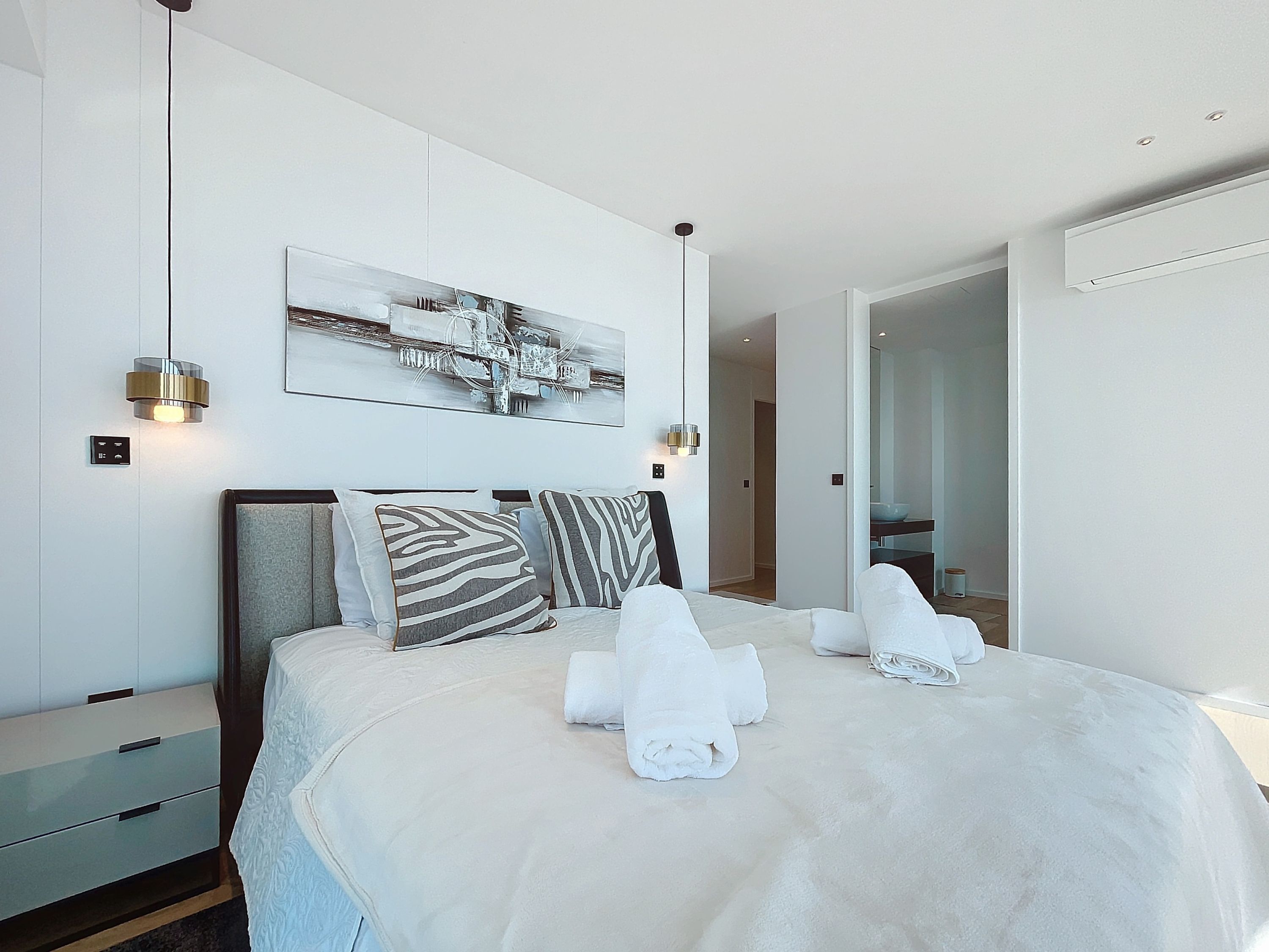 Un dormitorio moderno con una cama grande, dos mesitas de noche, una lámpara de pared y un cuadro abstracto de grandes dimensiones.