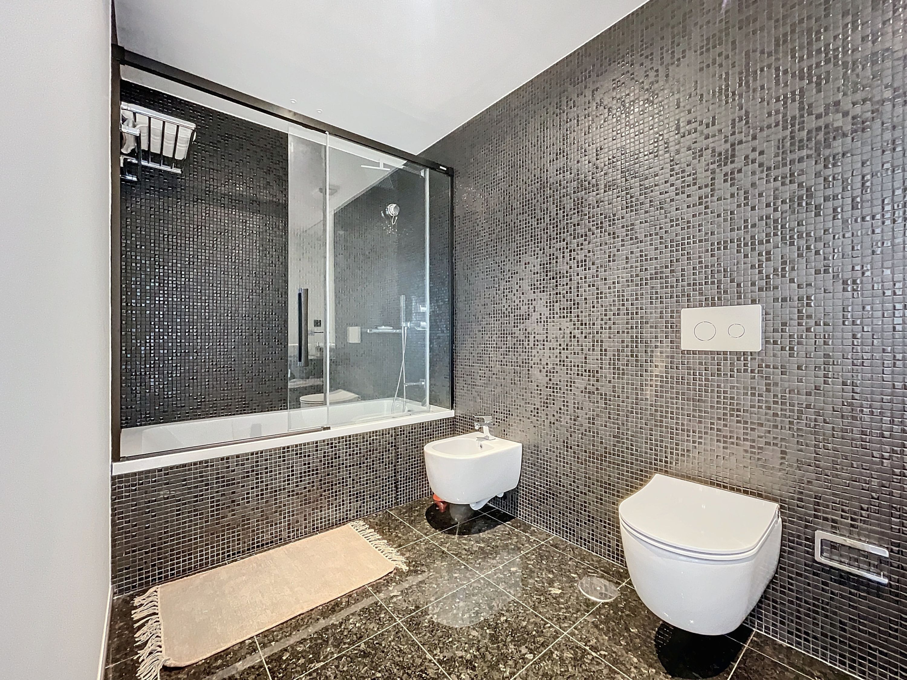 Ein modernes Badezimmer mit Duschkabine aus Glas, einem weißen Waschbecken und einer Toilette.