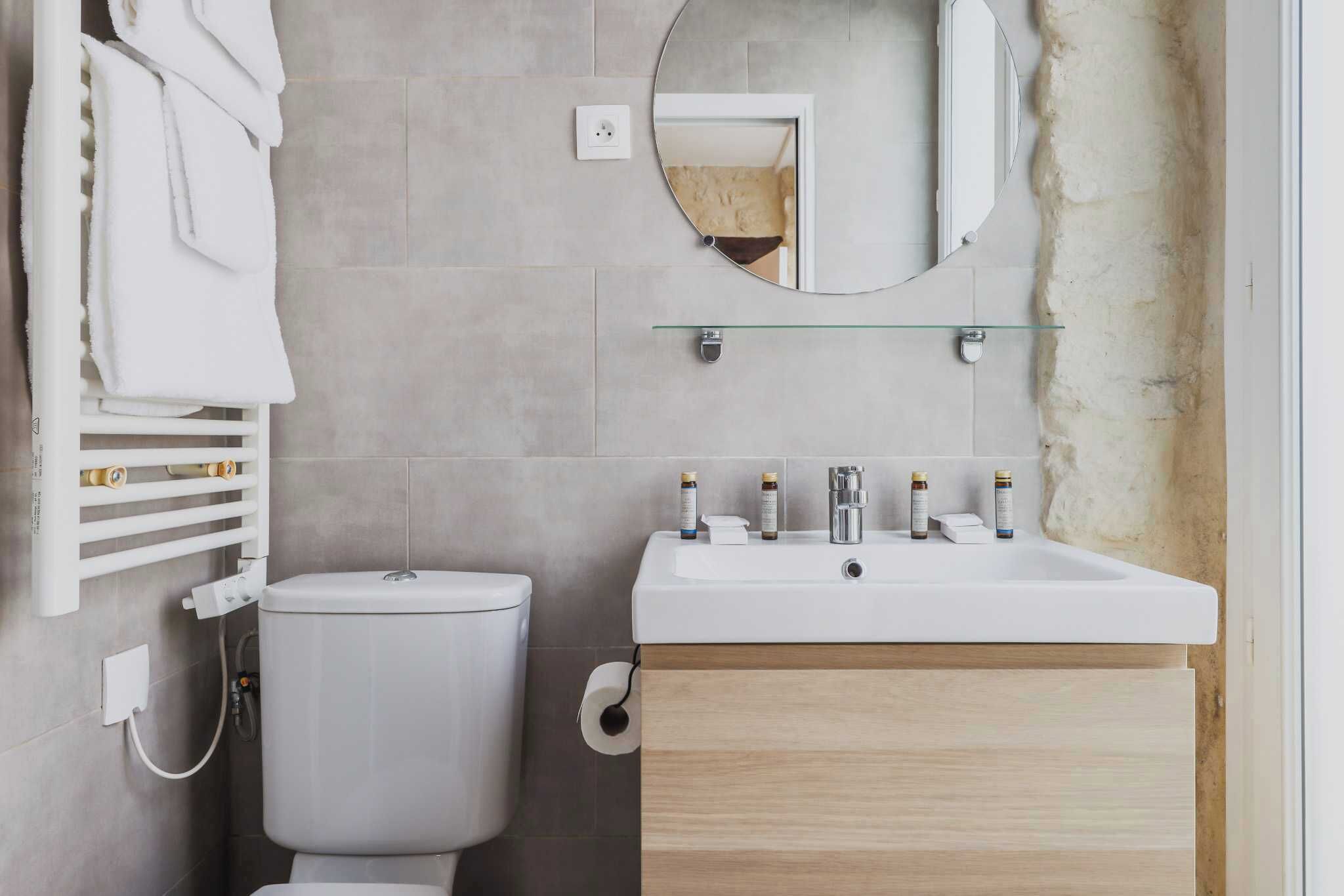 Ein modernes Badezimmer mit Toilette, Waschbecken und Spiegel darüber sowie einem Handtuchhalter mit Handtüchern.