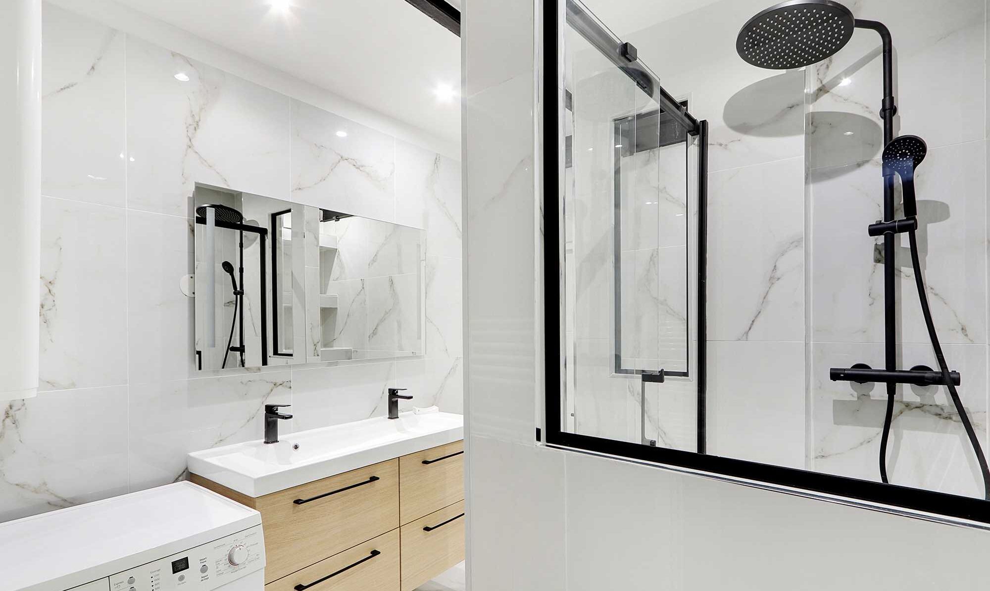 Un bagno moderno con cabina doccia in vetro, un vanità in marmo bianco e un grande specchio.