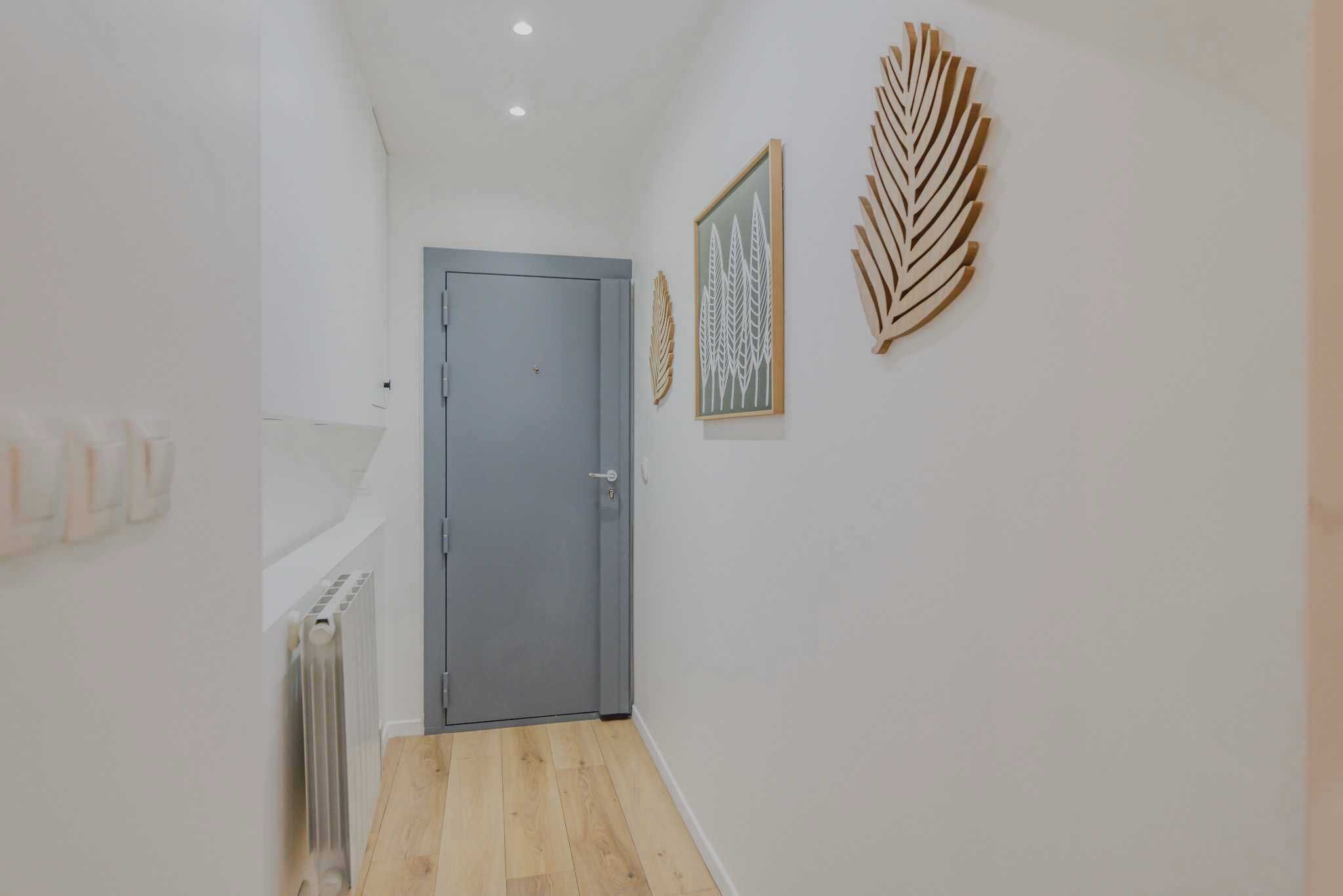A hallway with a grey door, white walls, and a radiator. There are two framed artworks on the wall.